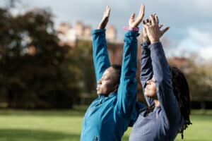 Two mature black women doing some stretching relaxing exercise in a park in autumn.