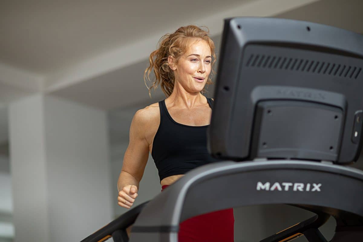 A woman is running on a treadmill in a gym.